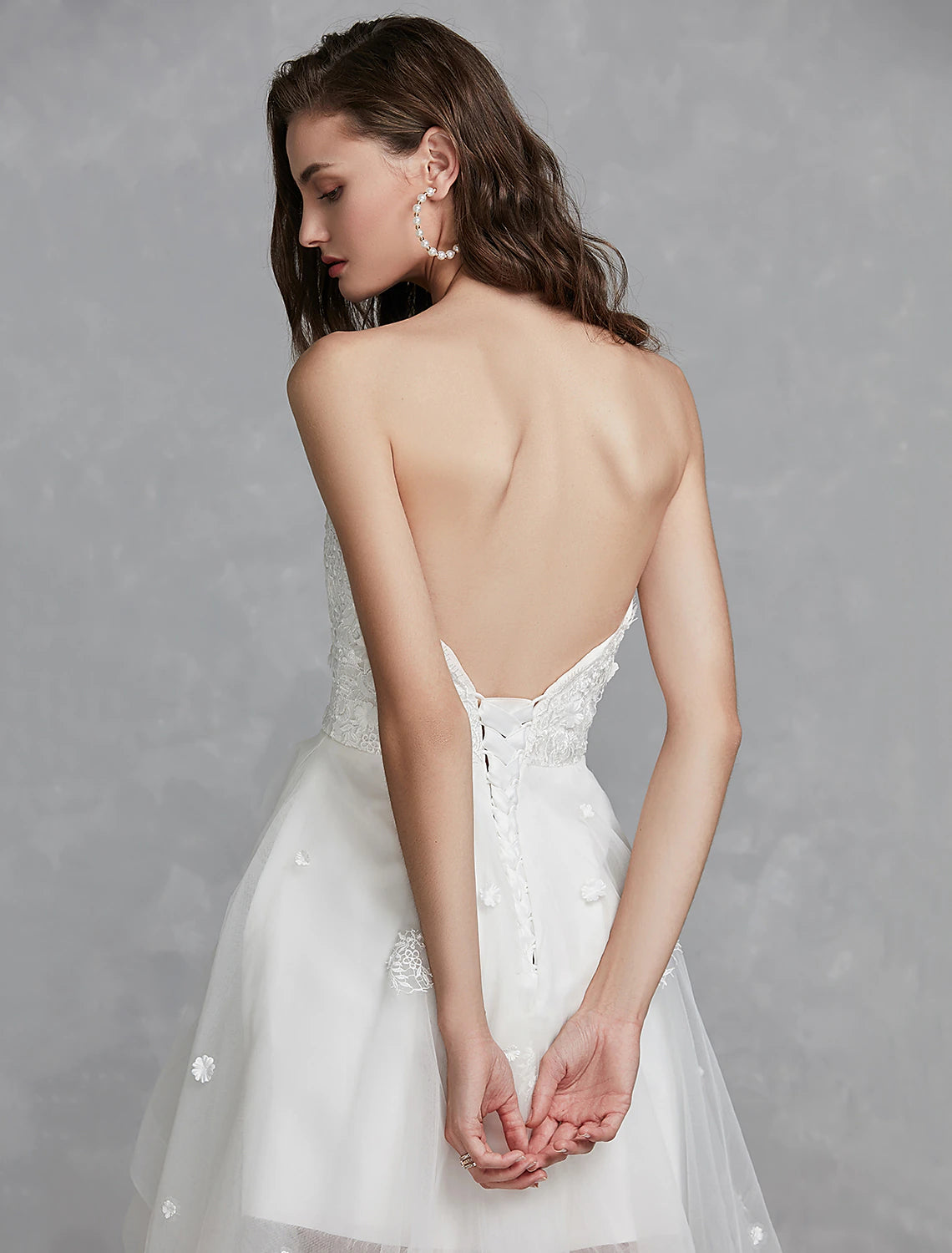 Elegant A-line sweetheart strapless white bridal gown with lace appliques and asymmetrical hem.