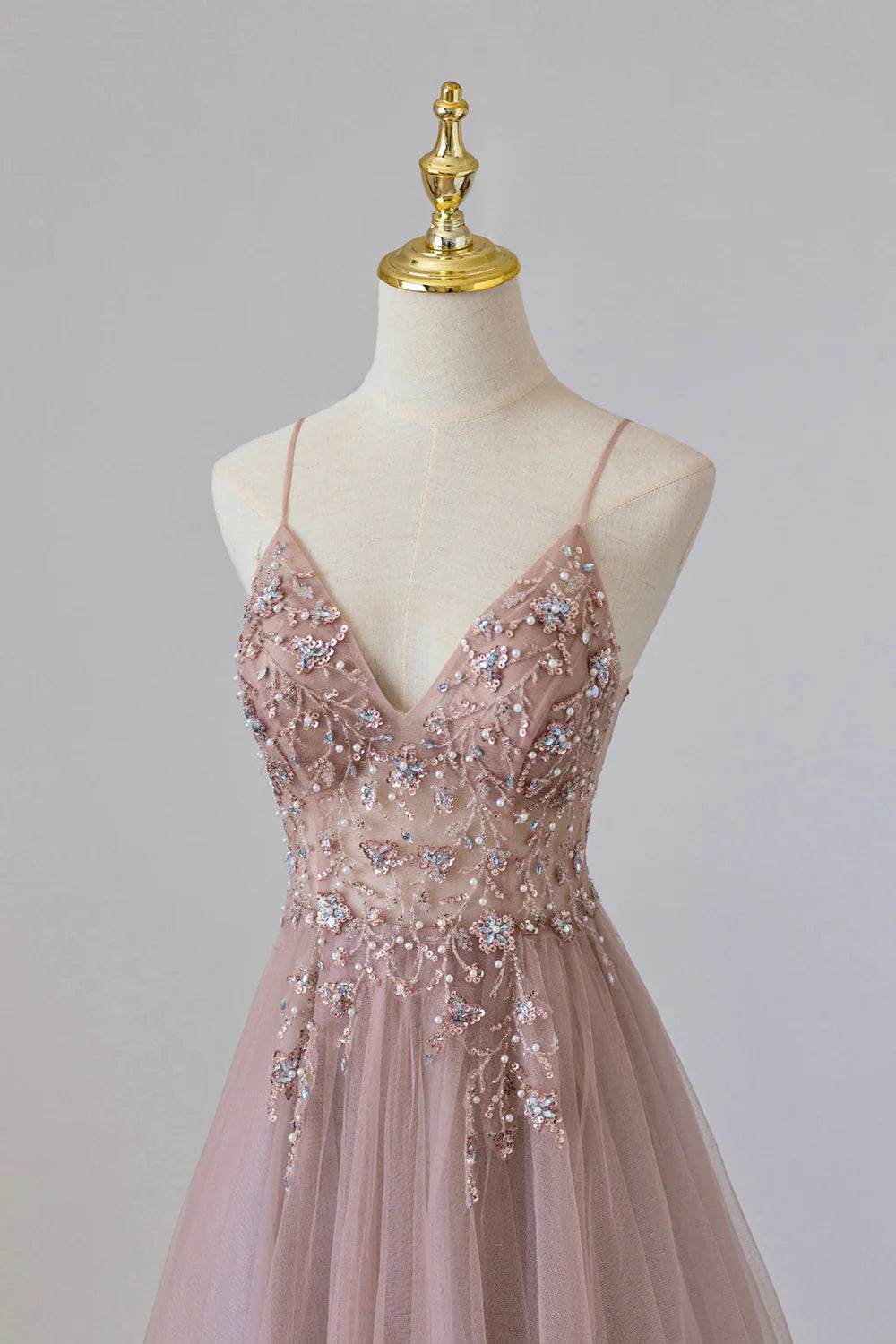 Back view of a woman wearing an A-line tulle long spaghetti strap evening gown.