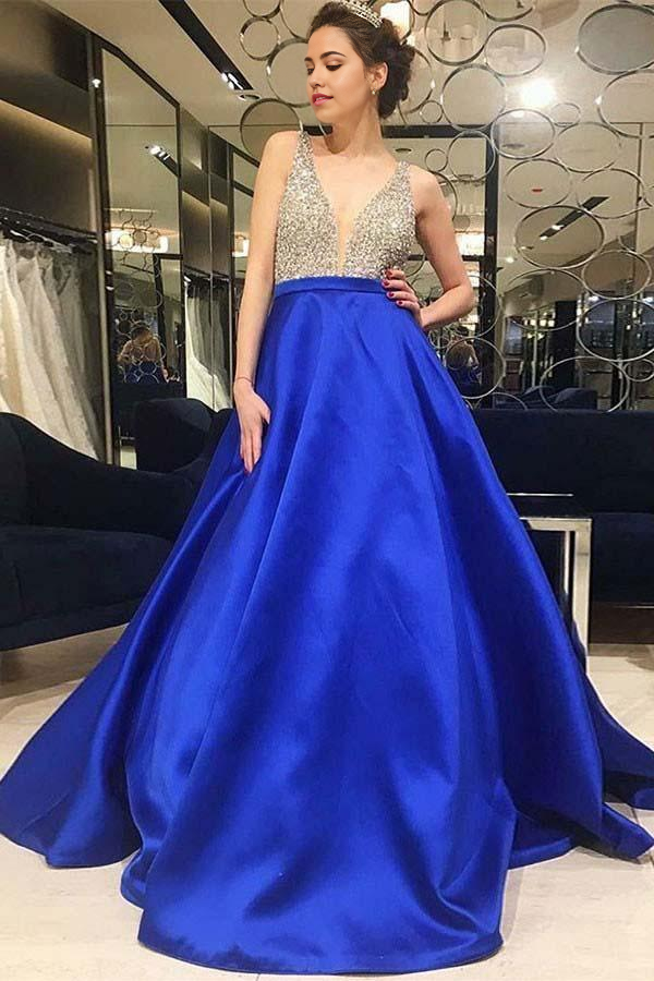 Model wearing a royal blue A-line satin prom dress with V-neck and beading.