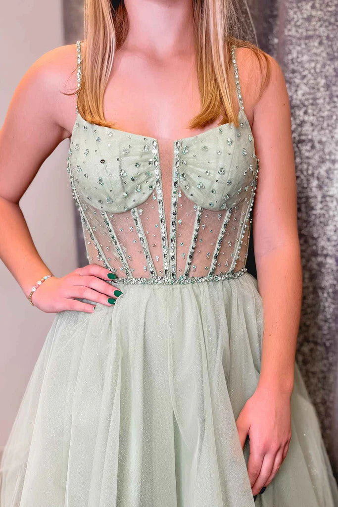 Full view of a woman in a shimmering sage green A-line tulle prom dress with V-neck.