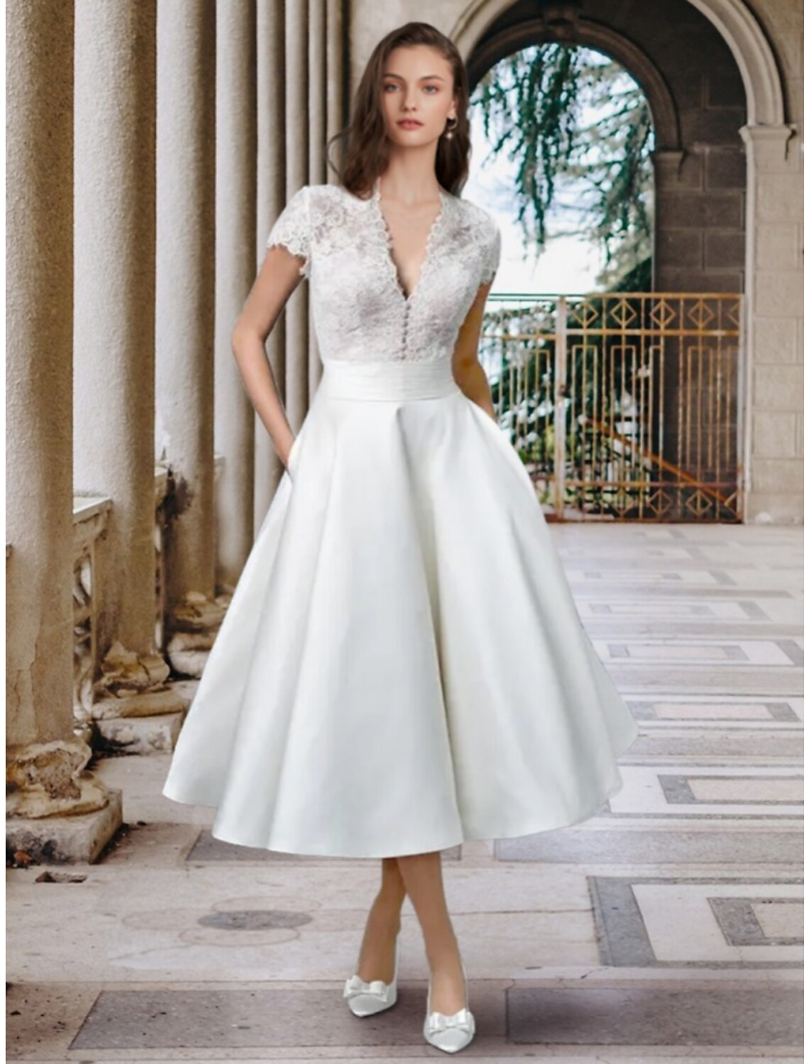 Model wearing an elegant A-line V-neck short sleeve satin tea length wedding dress with pleats.