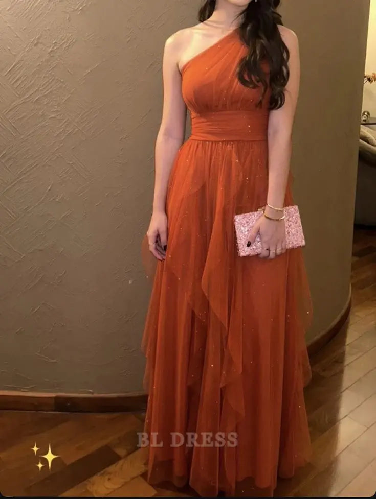 Model wearing a rust orange A-line one-shoulder tulle formal dress.