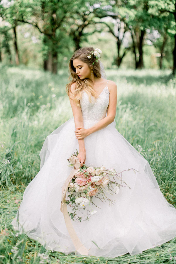 Bride in elegant A-line V-neck wedding dress with forest background.