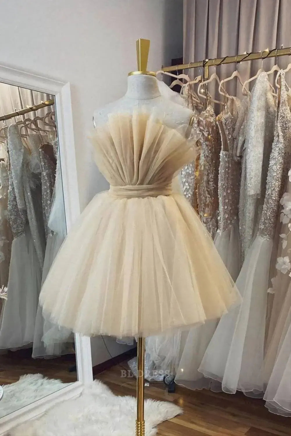 Model wearing a champagne A-line backless short tulle dress with a large bow detail on the back.