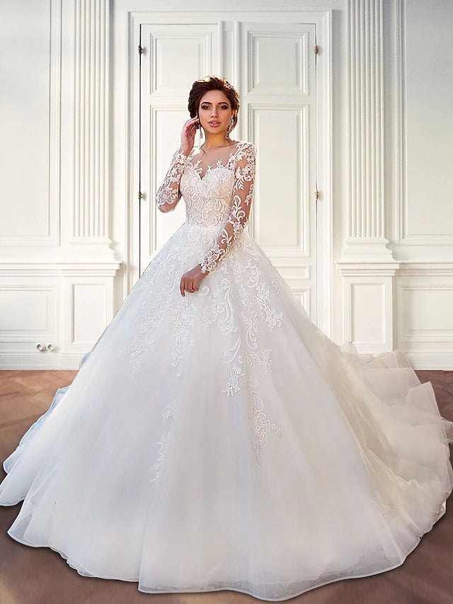 Bride wearing an elegant white ball gown wedding dress with long illusion lace sleeves and a court train.