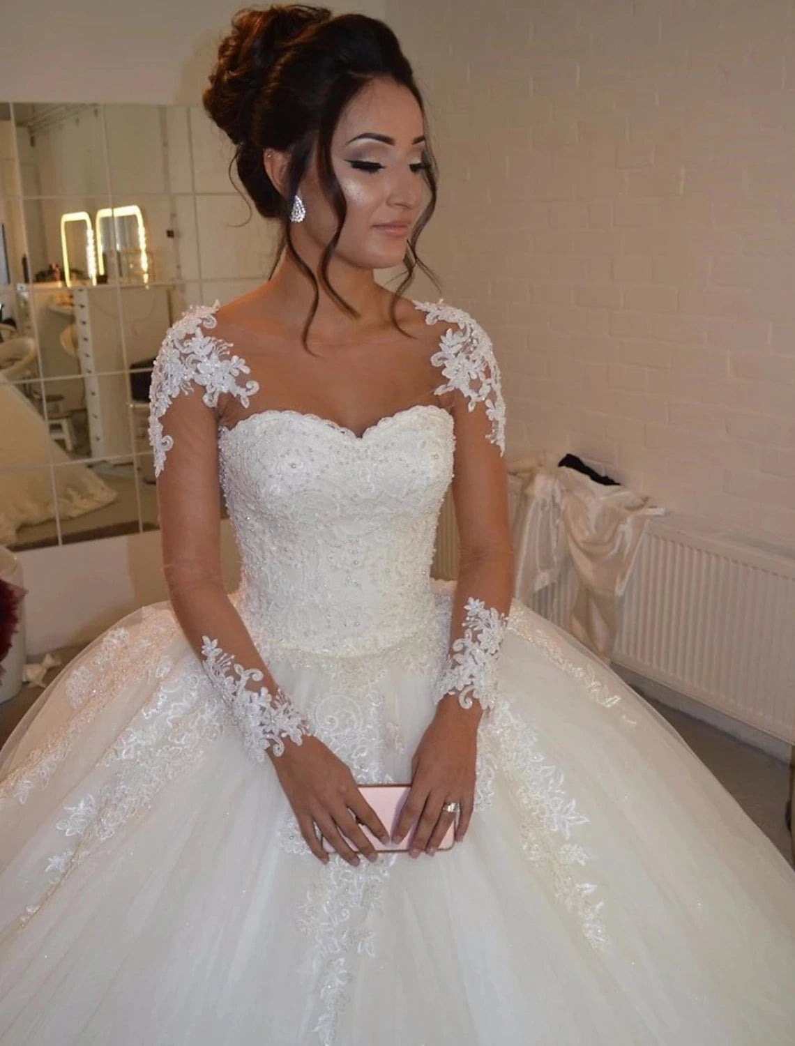 Model wearing an elegant white lace ball gown wedding dress with long sleeves and sweetheart neckline.