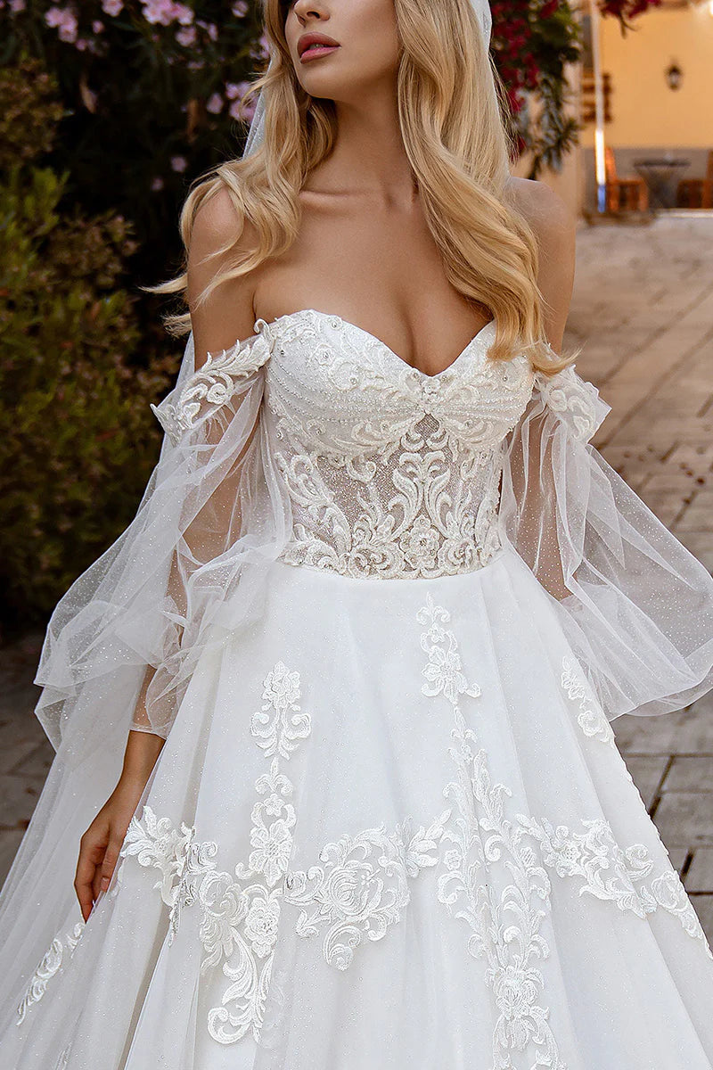 Close-up of the lace appliques and long sleeves on a white sweetheart ball gown wedding dress.