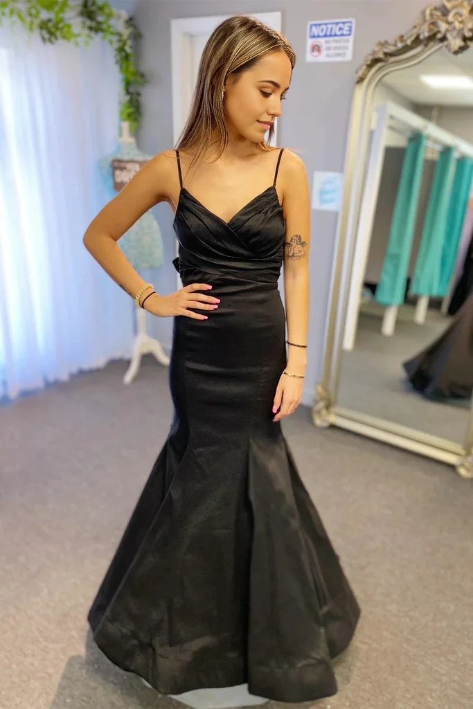 Model wearing a black mermaid prom dress with surplice V-neck, pleated bodice, and a bow detail.