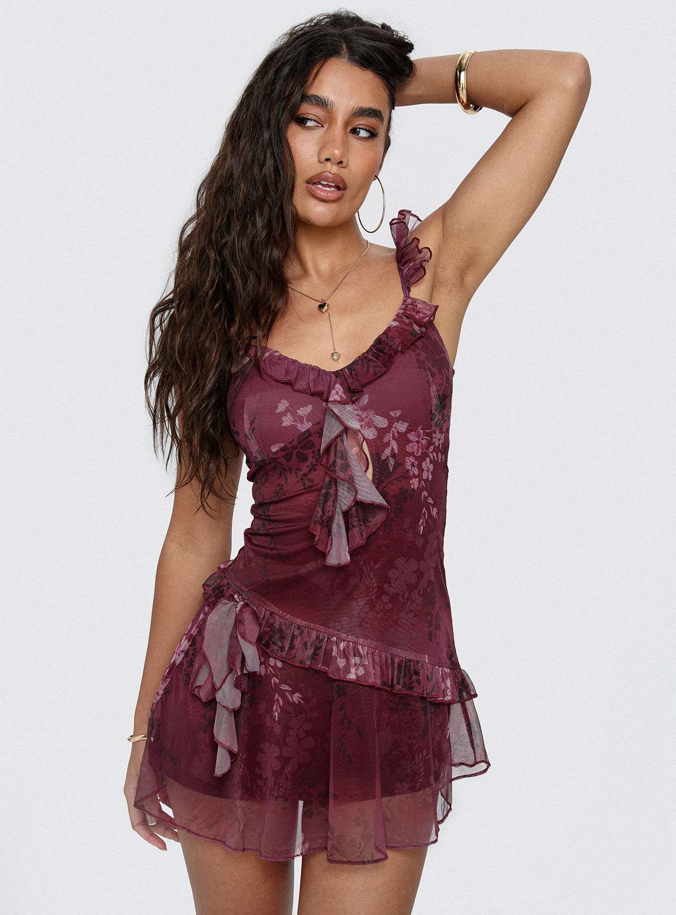 Woman posing in a burgundy floral mesh mini dress with ruffle straps and V-neck.