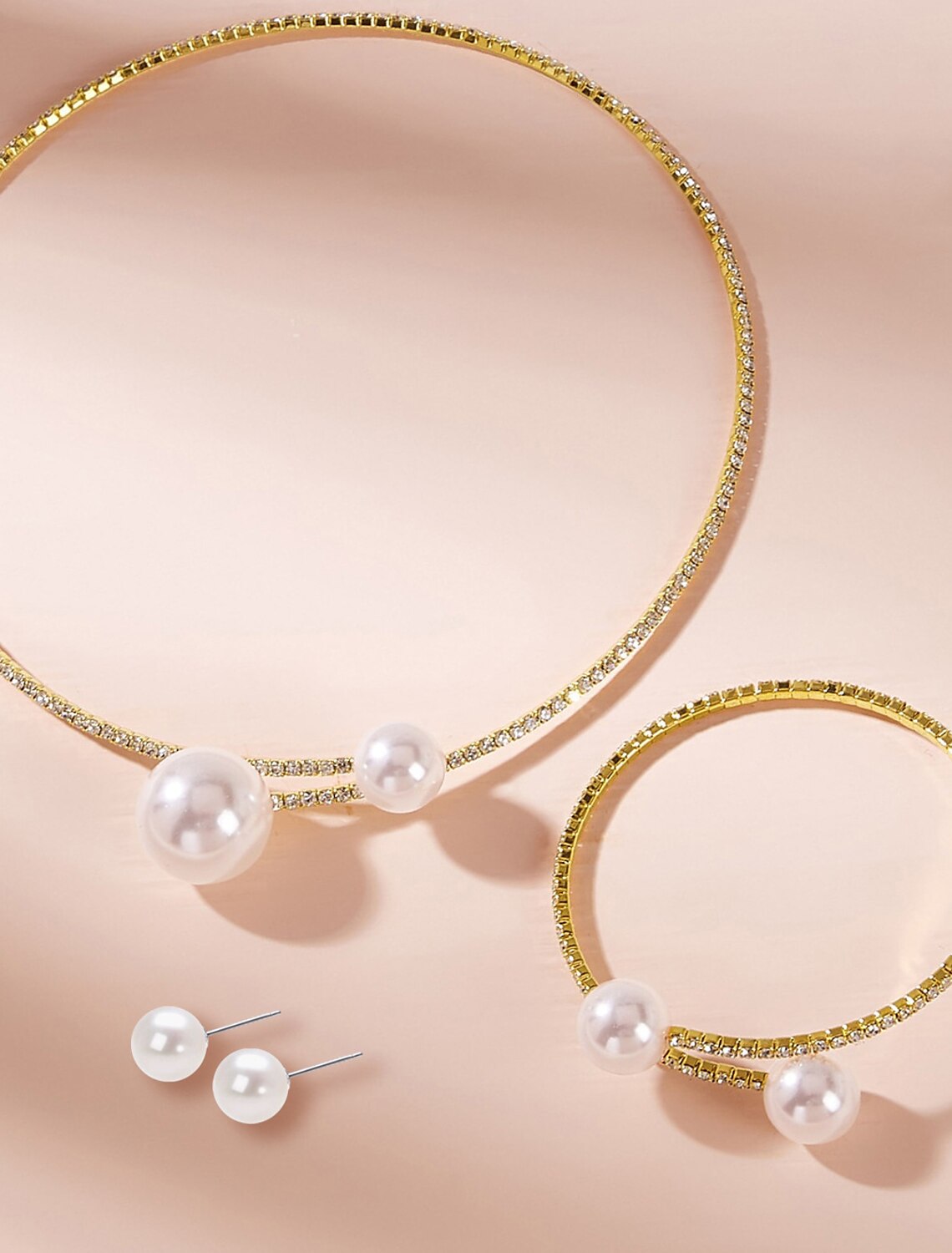 Elegant bridal jewelry set featuring an imitation pearl and rhinestone necklace, earrings, and bracelet on a white.