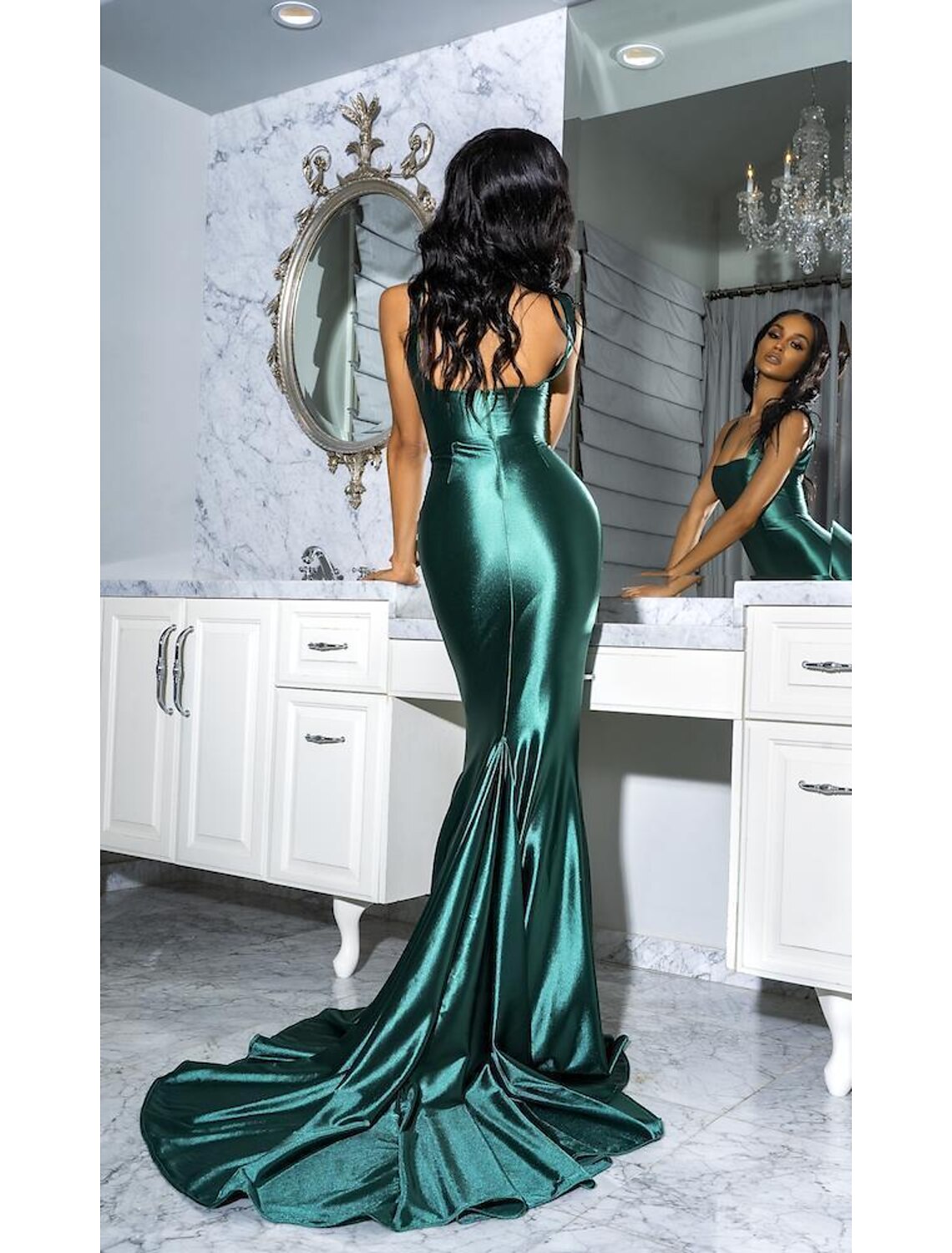 Woman wearing an emerald green mermaid trumpet gown with spaghetti straps and a court train.