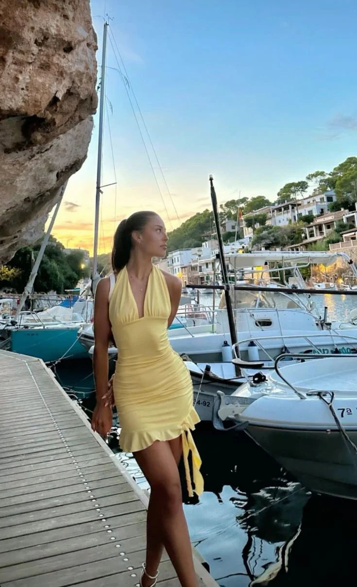 Model wearing a yellow halter ruched homecoming dress with deep V-neck and ruffle hem.