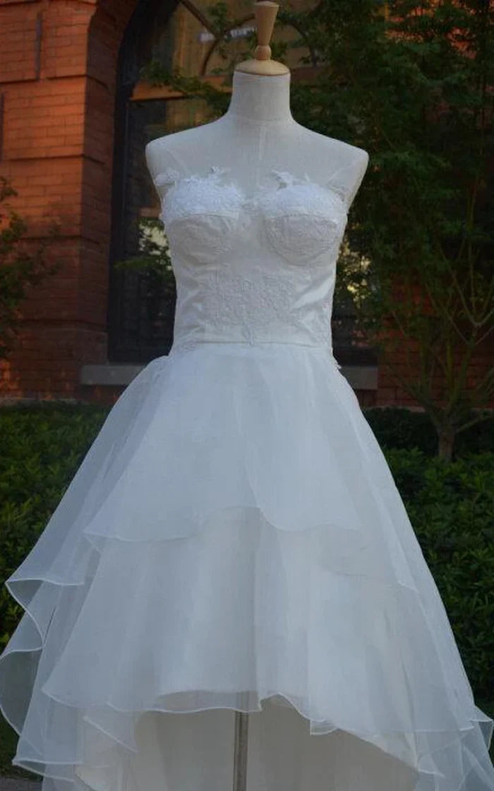 Back view of a white high-low chiffon wedding dress with lace-up detailing and tiered ruffles.