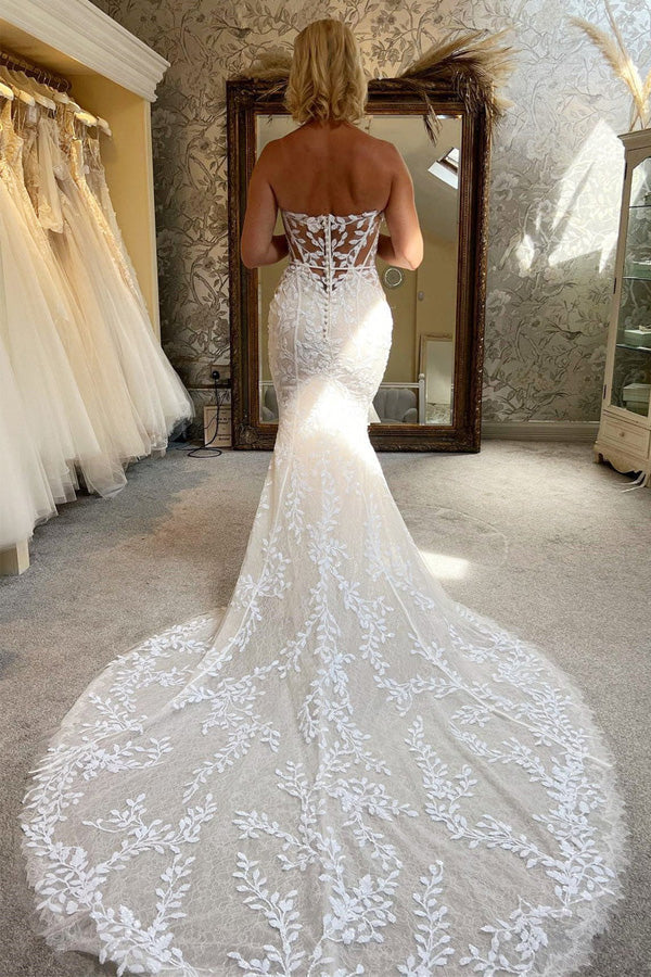 Side view of an ivory lace mermaid bridal gown with a flowing train.
