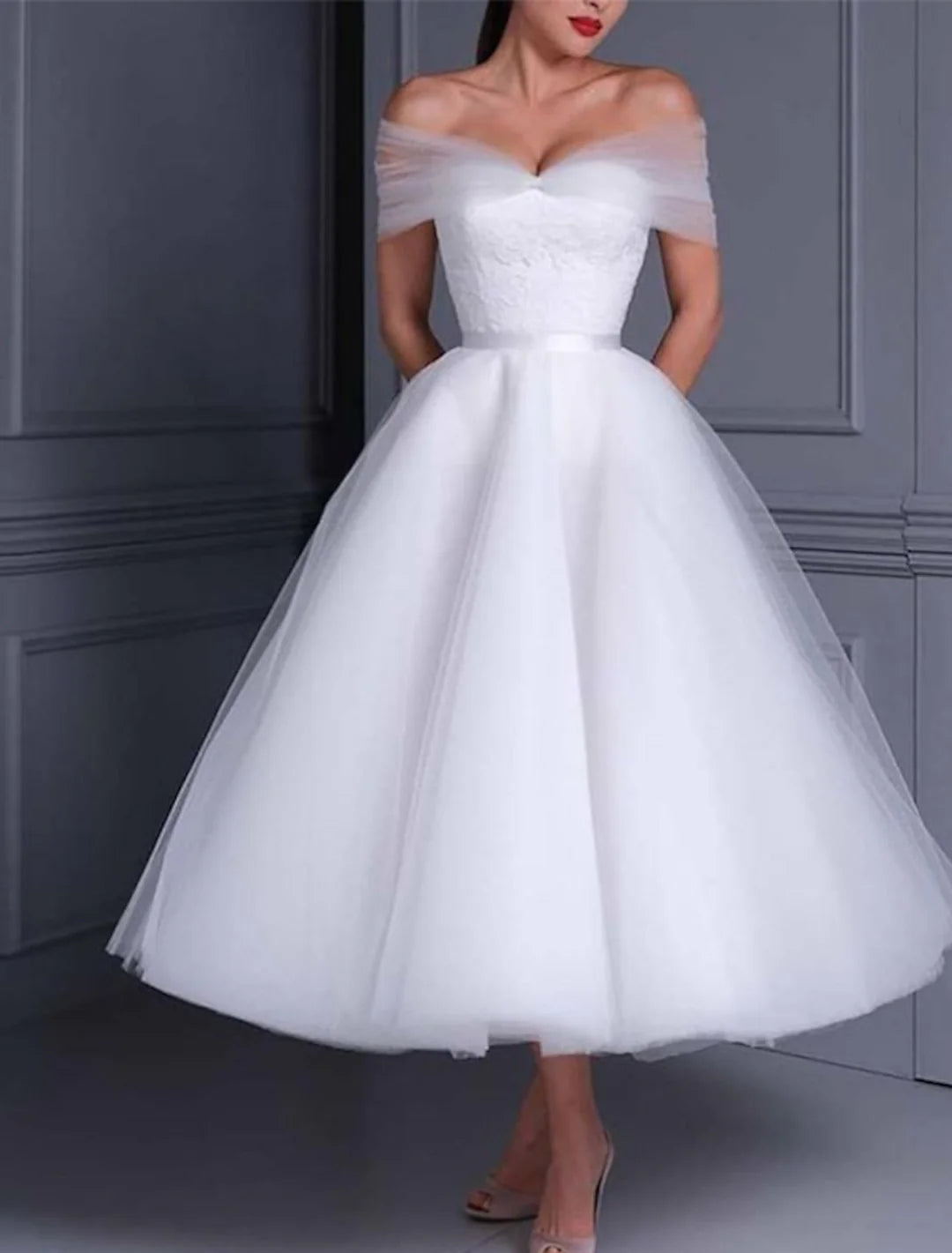 Model wearing an elegant white lace ball gown wedding dress with an off-the-shoulder neckline and ankle-length skirt.