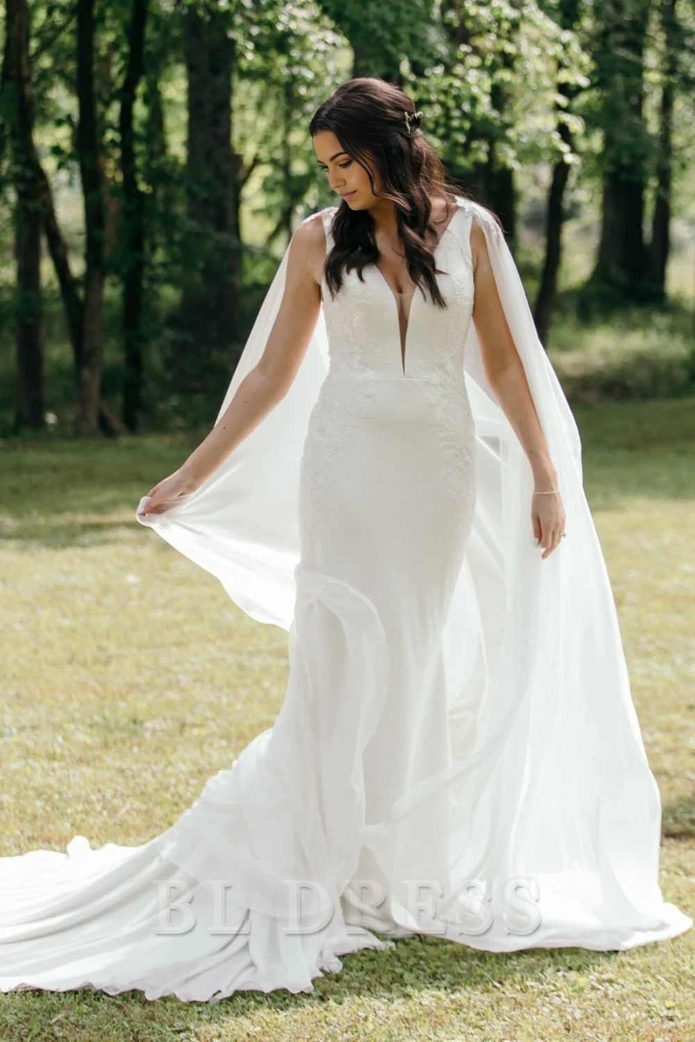 Back view of a bride in a white mermaid wedding gown with a long, elegant cape.