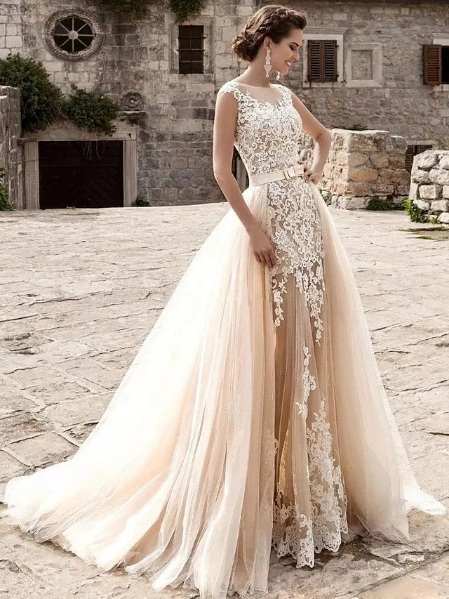 Front view of a bride wearing an elegant white mermaid lace wedding dress with cap sleeves and an illusion neckline.
