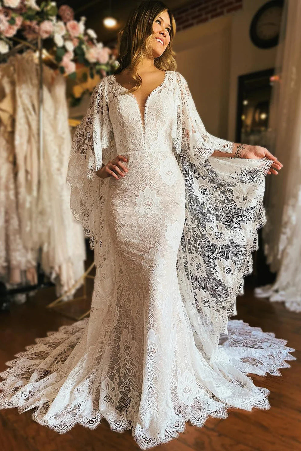 Elegant ivory mermaid wedding dress with long lace sleeves, appliques, and a flowing cape.