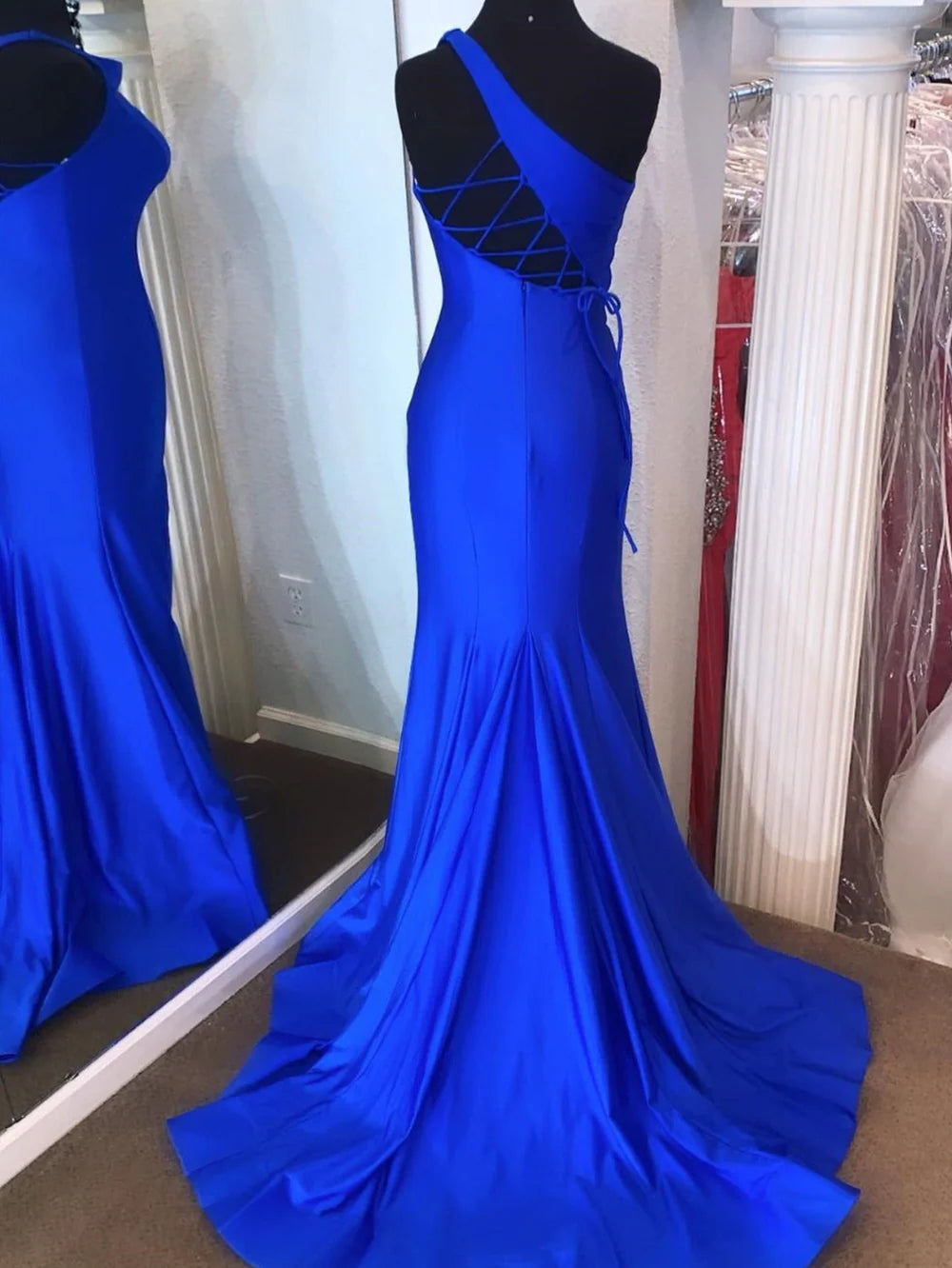 Back view of a woman in a mermaid one-shoulder long prom dress, showcasing the elegant train.