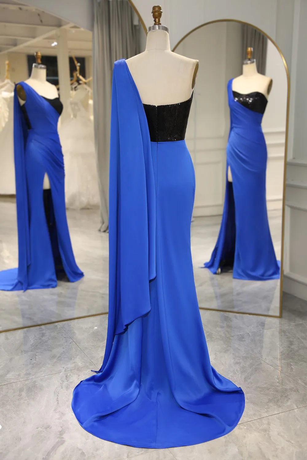 Back view of royal blue one-shoulder mermaid dress with flowing shawl.
