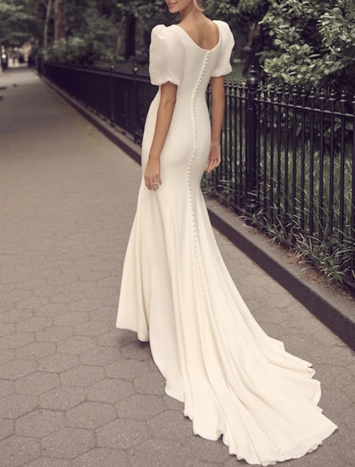 Side view of a bride in a white satin trumpet wedding gown with a flowing train.