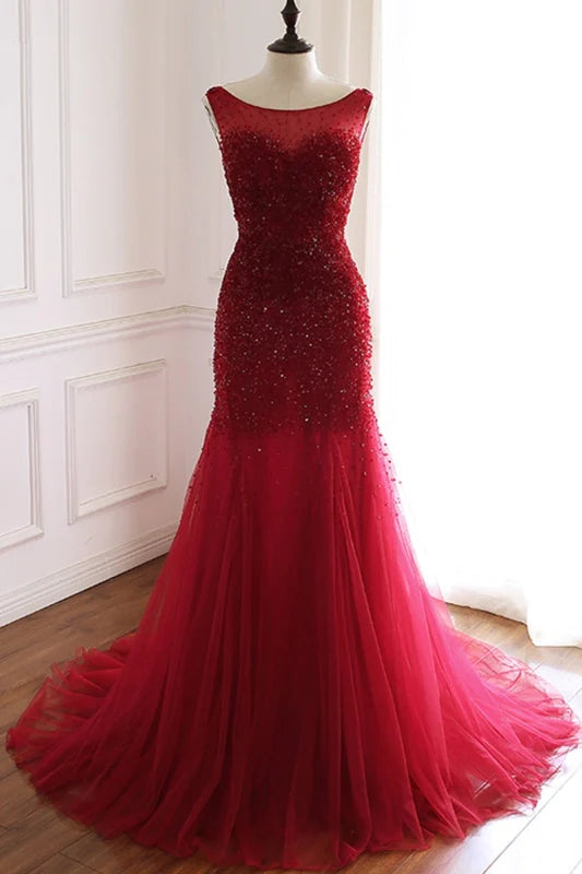 Woman wearing a long mermaid tulle prom dress with an open back and intricate beading.