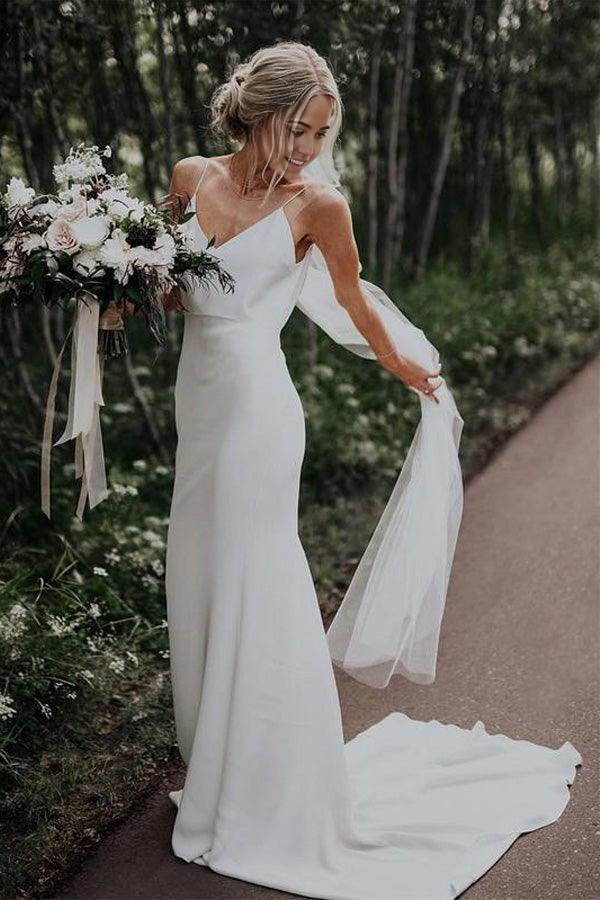 Front view of a woman wearing an elegant white mermaid V-neck wedding dress with spaghetti straps on a beach.