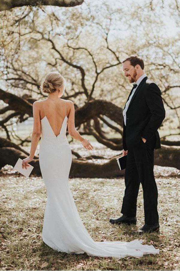 Side view of a woman in a white mermaid wedding dress with spaghetti straps and a V-neck, posing outdoors.