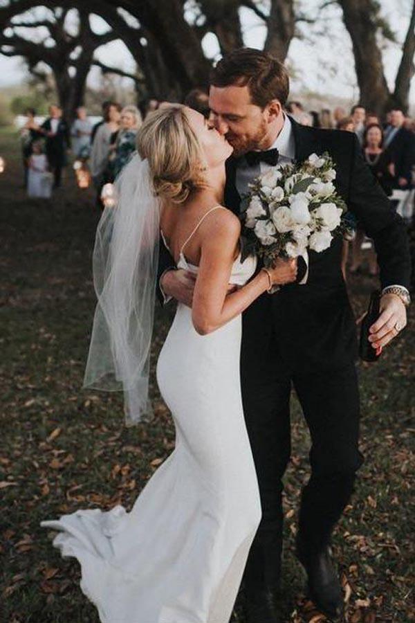 Back view of a woman showcasing the backless design of a white mermaid wedding dress with spaghetti straps.