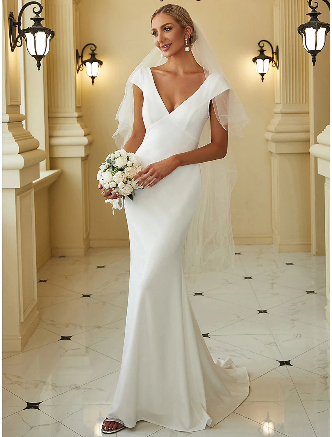 Woman wearing an elegant white mermaid V-neck cap sleeve wedding dress with draping.