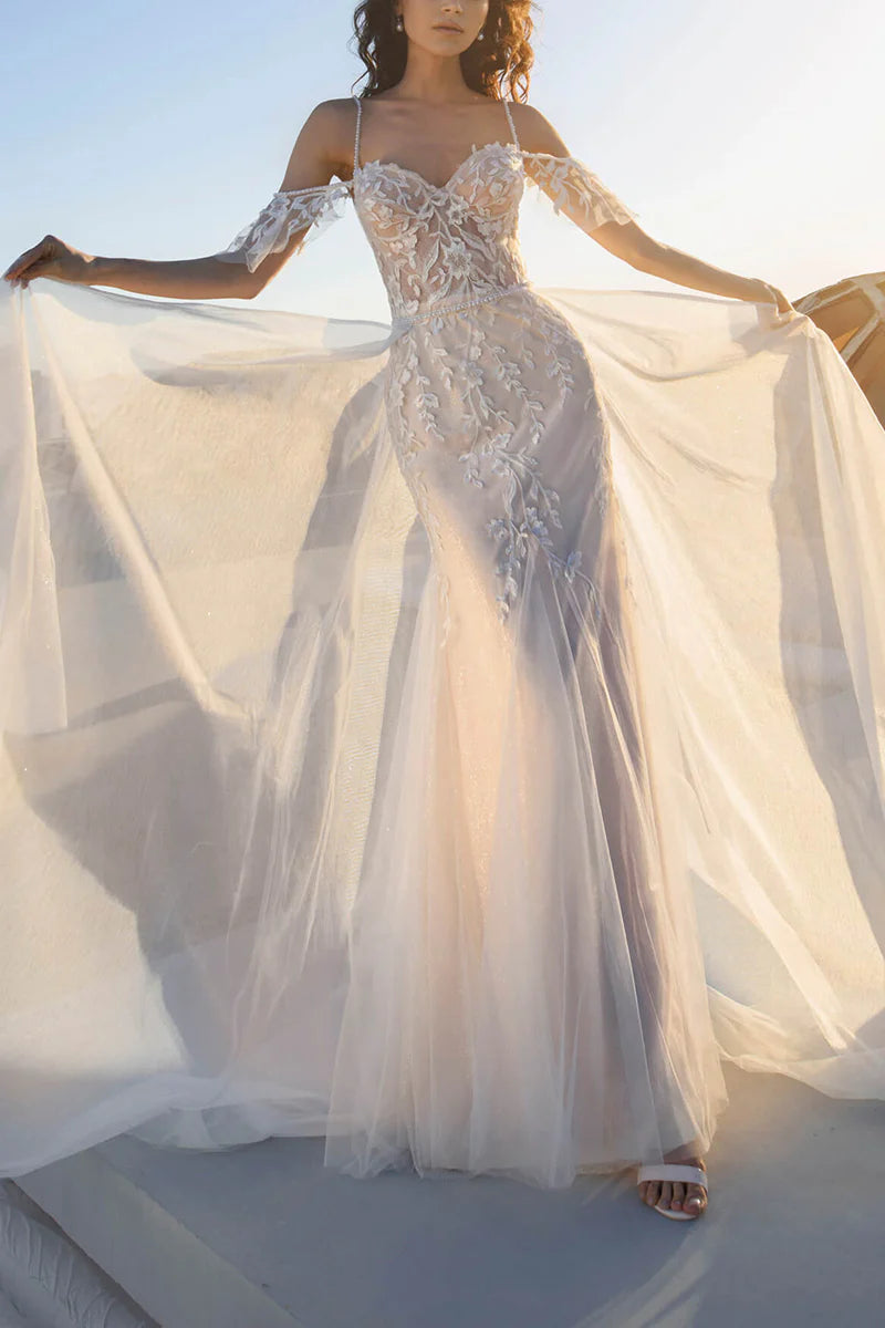 Mermaid wedding dress with flowing train and spaghetti straps.
