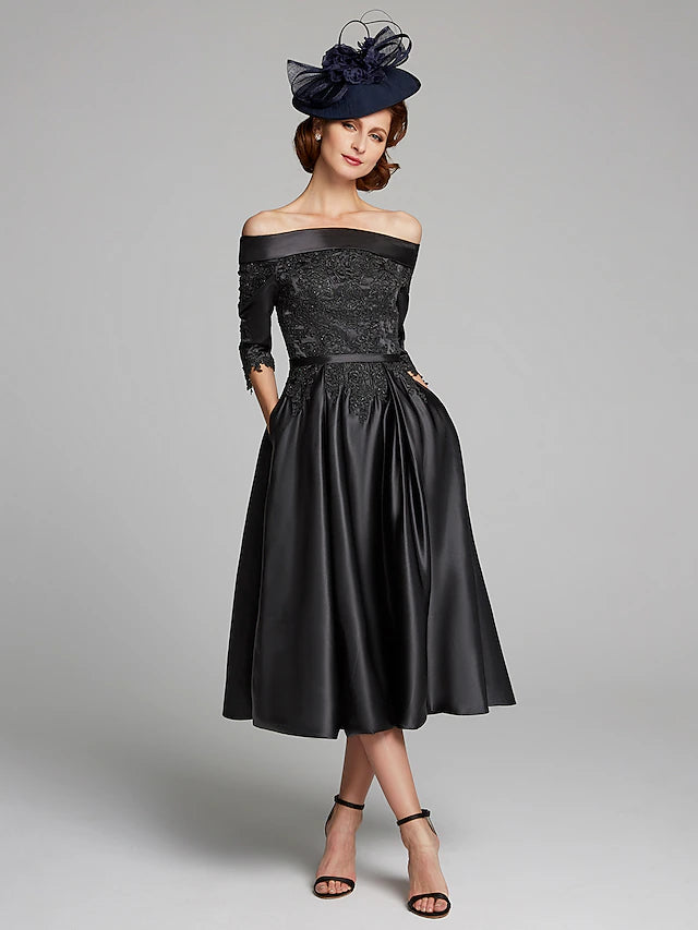 Woman wearing an elegant navy A-line off-shoulder tea-length Mother of the Bride dress with 3/4 lace sleeves.