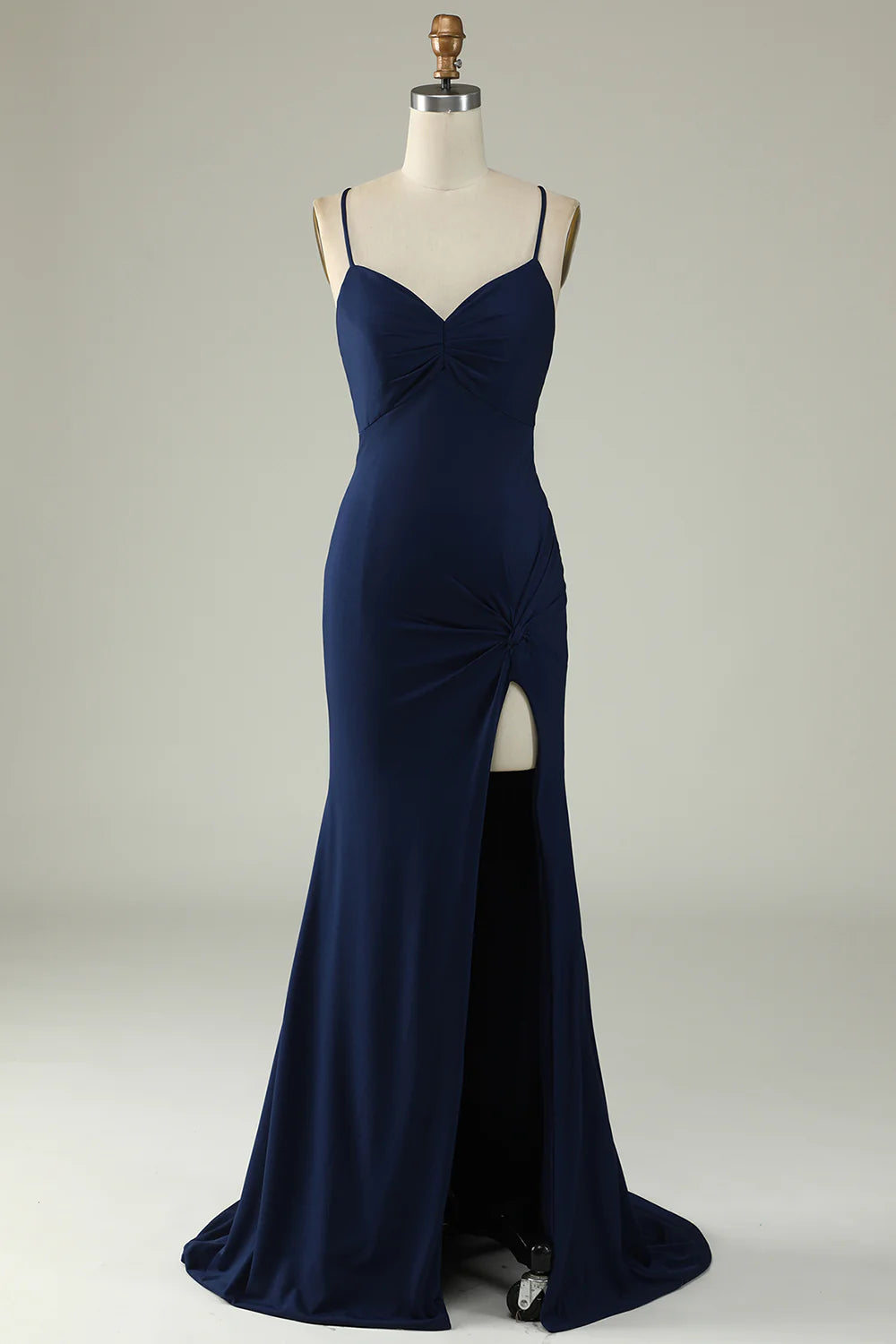 Woman wearing an elegant navy mermaid long prom dress with spaghetti straps and a high slit.