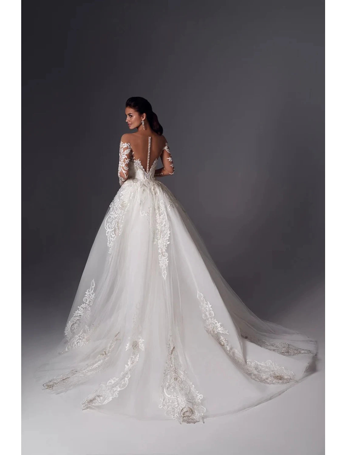 Side profile of an off-shoulder bridal gown with long sleeves and intricate appliques.