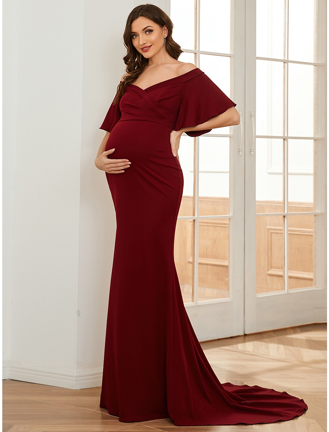 Woman in a red off-shoulder short sleeve mermaid maternity dress with ruched details.