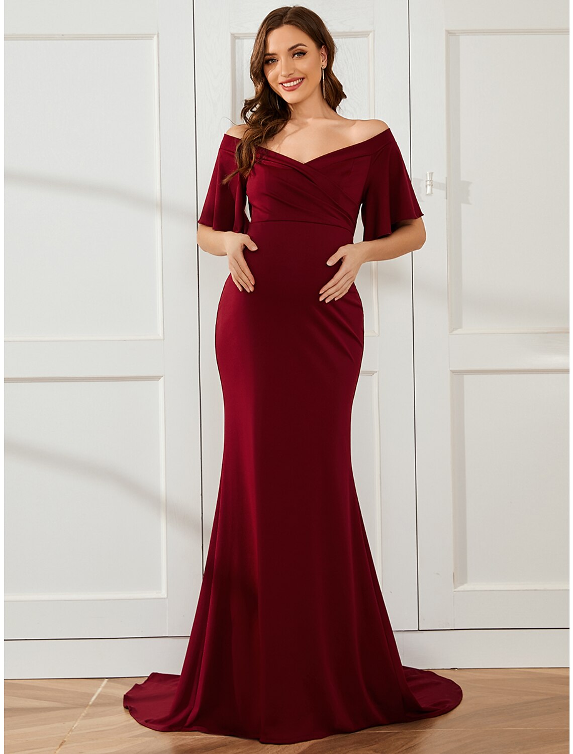Side view of a woman in a red off-shoulder maternity gown, showcasing the court train.