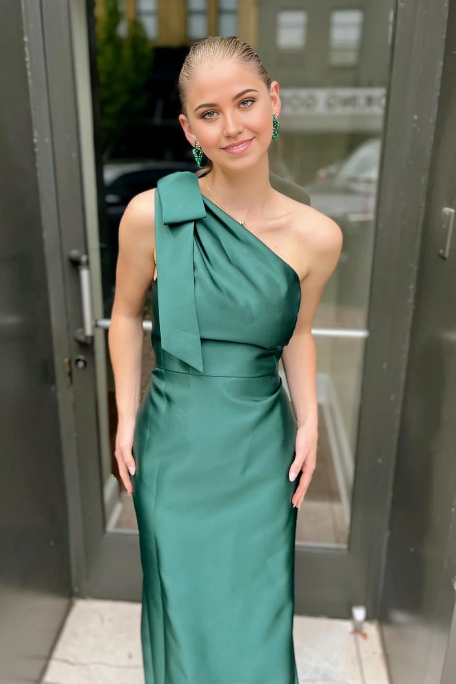 Elegant one-shoulder green satin prom dress with a bow detail and pleats.