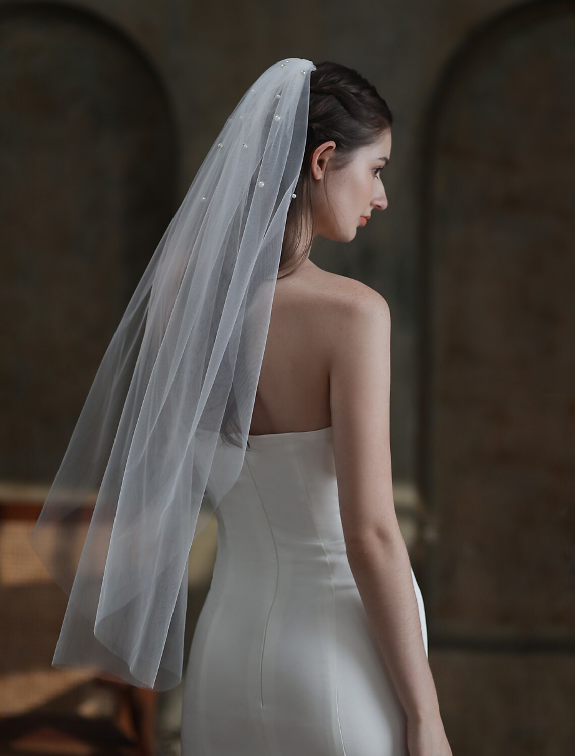 Back view of a bride wearing an elegant fingertip pearl wedding veil.