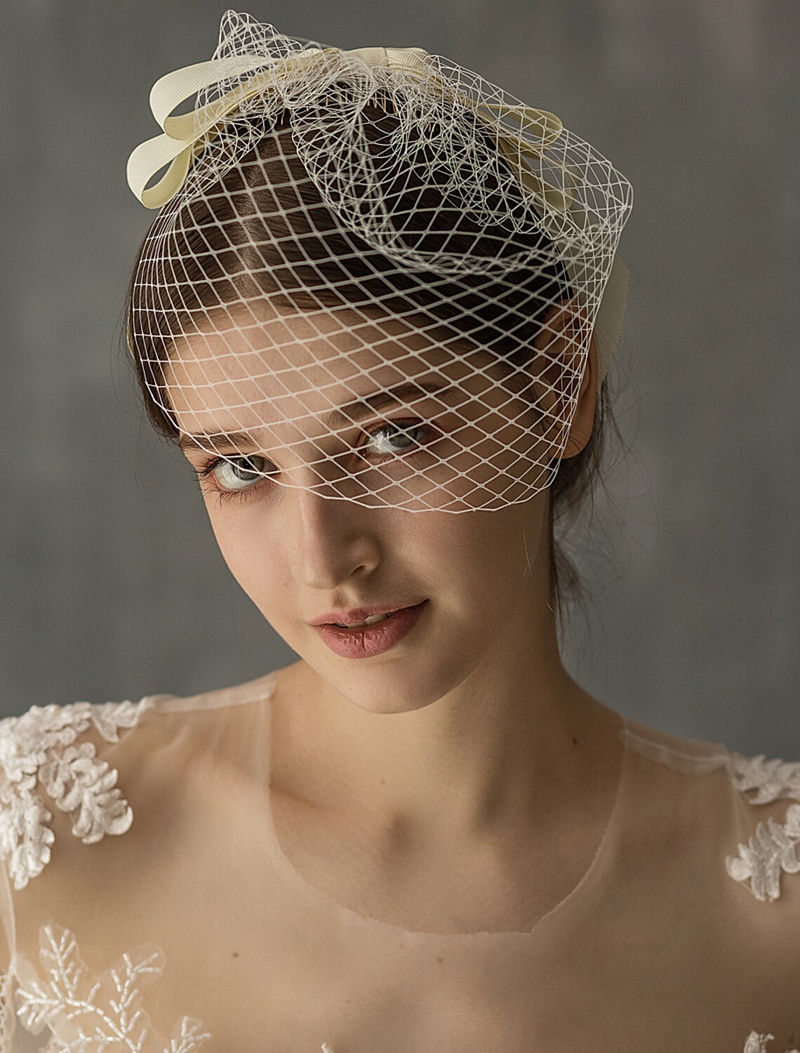 Side view of a bride wearing a one-tier birdcage veil with tulle and ribbon.