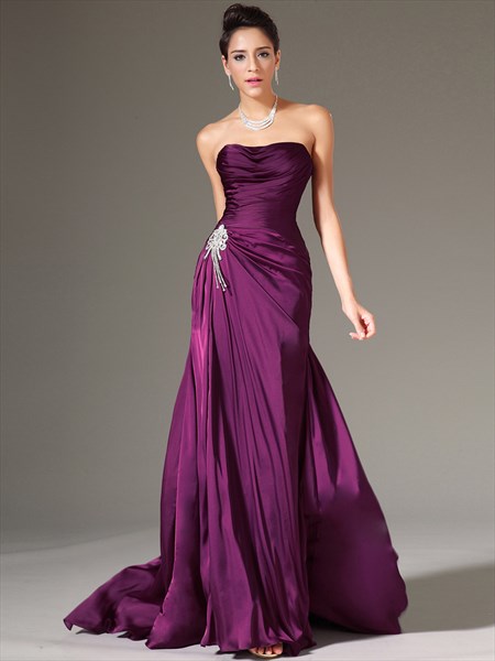 Full-length view of a woman wearing a purple strapless ruched sheath prom dress with crystal embellishments.