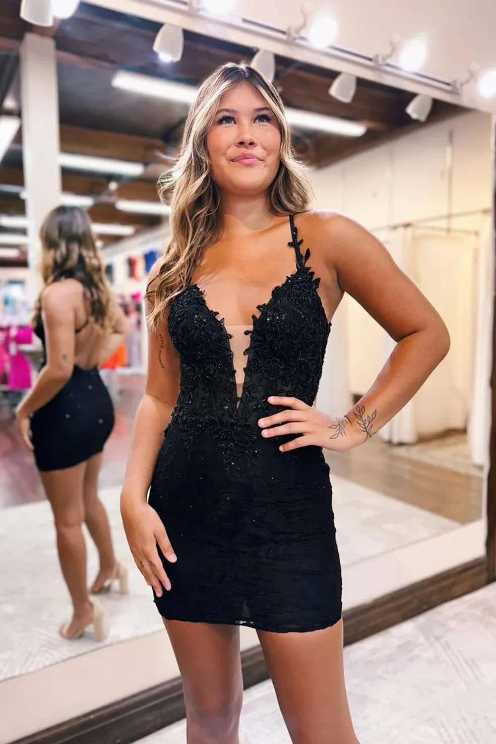 Model wearing a black sheath bodycon homecoming dress with spaghetti straps and appliques.