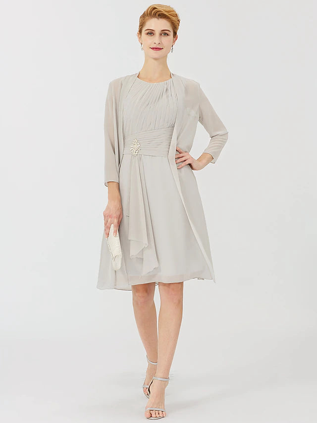 Woman wearing an elegant knee-length sheath dress with a jewel neck and 3/4 sleeves, featuring a crystal brooch.