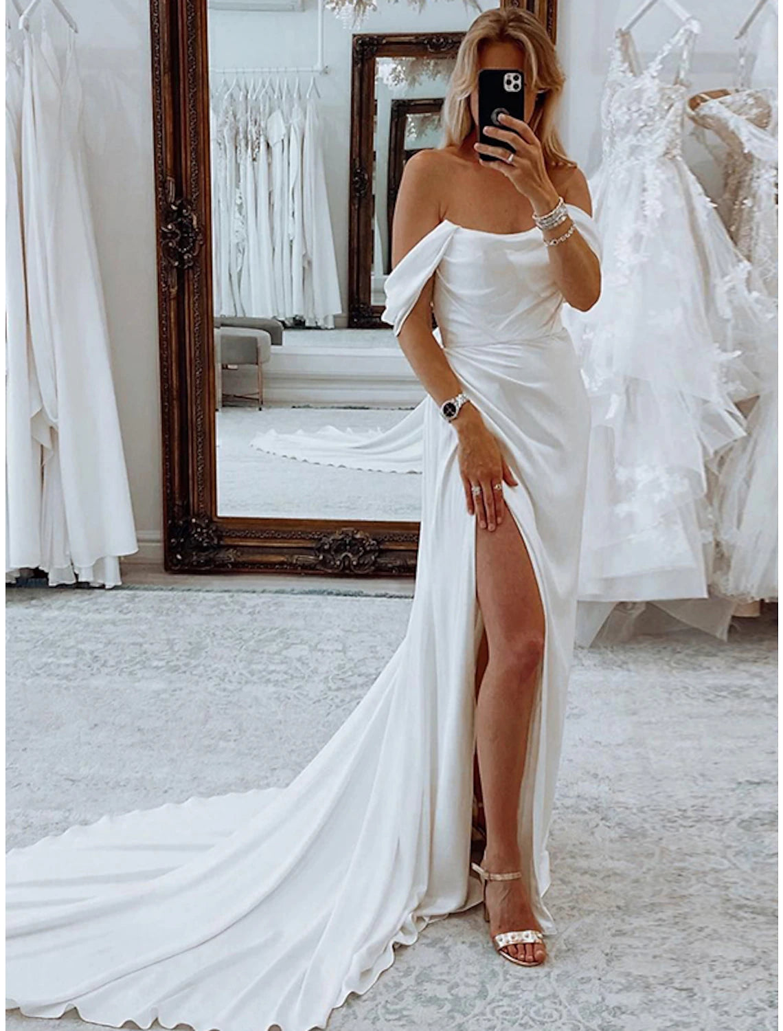 Model wearing an elegant off-shoulder sheath wedding dress with ruched details and a court train.