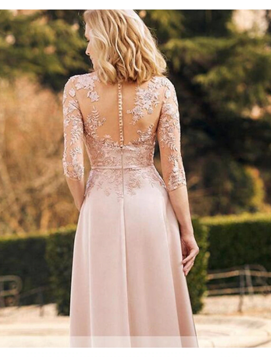 Woman posing in an elegant floor-length sheath satin mother of the bride dress with long sleeves and a jewel neck.