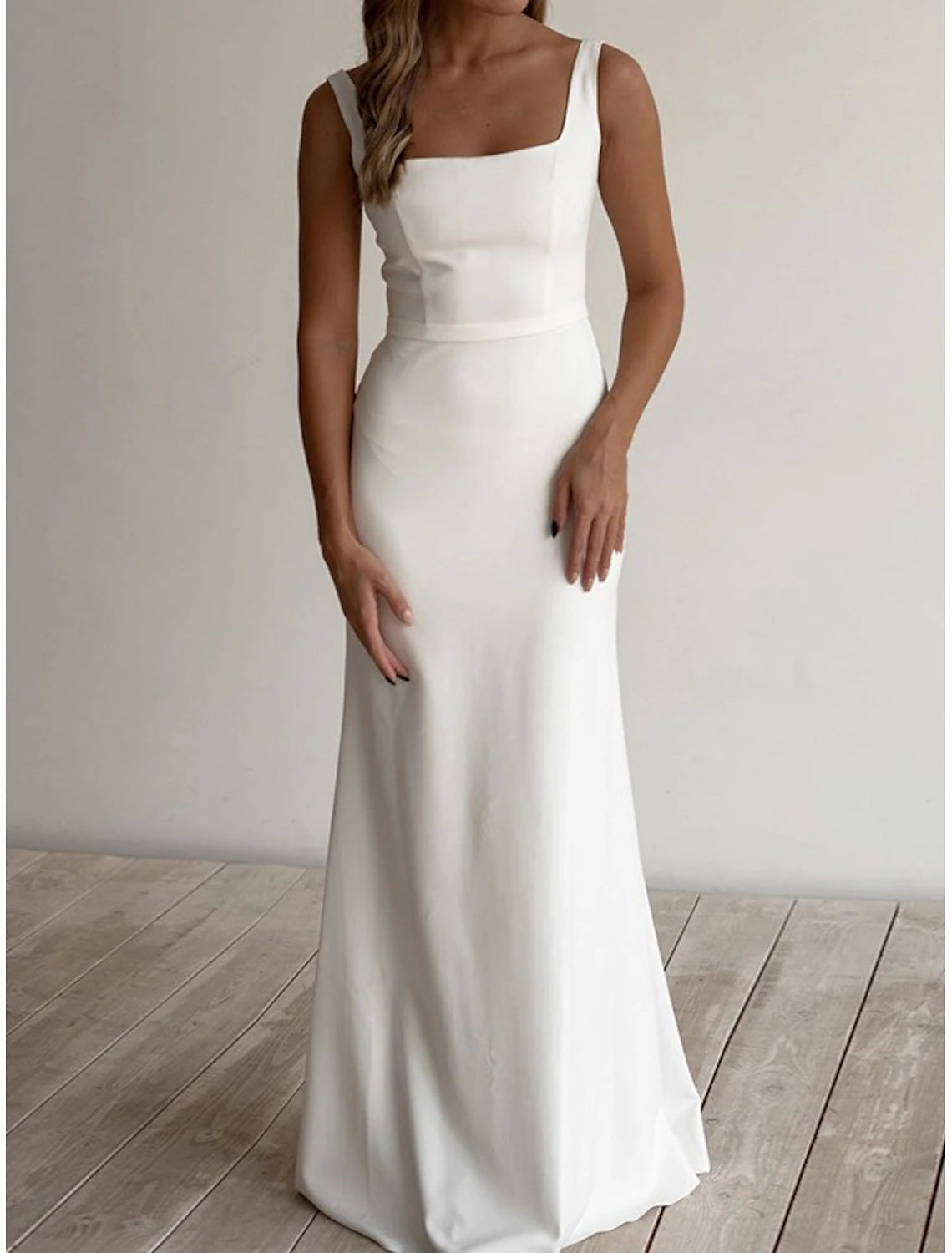 Model wearing an elegant white sheath wedding dress with a square neck and sash, perfect for a beach ceremony.