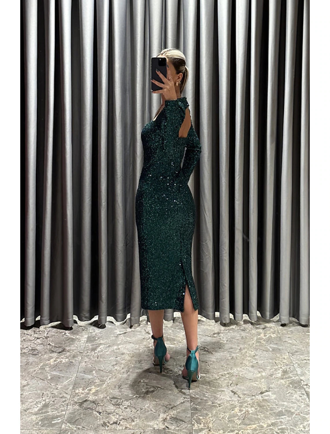 Side view of a woman wearing a black sequined tea length evening gown.