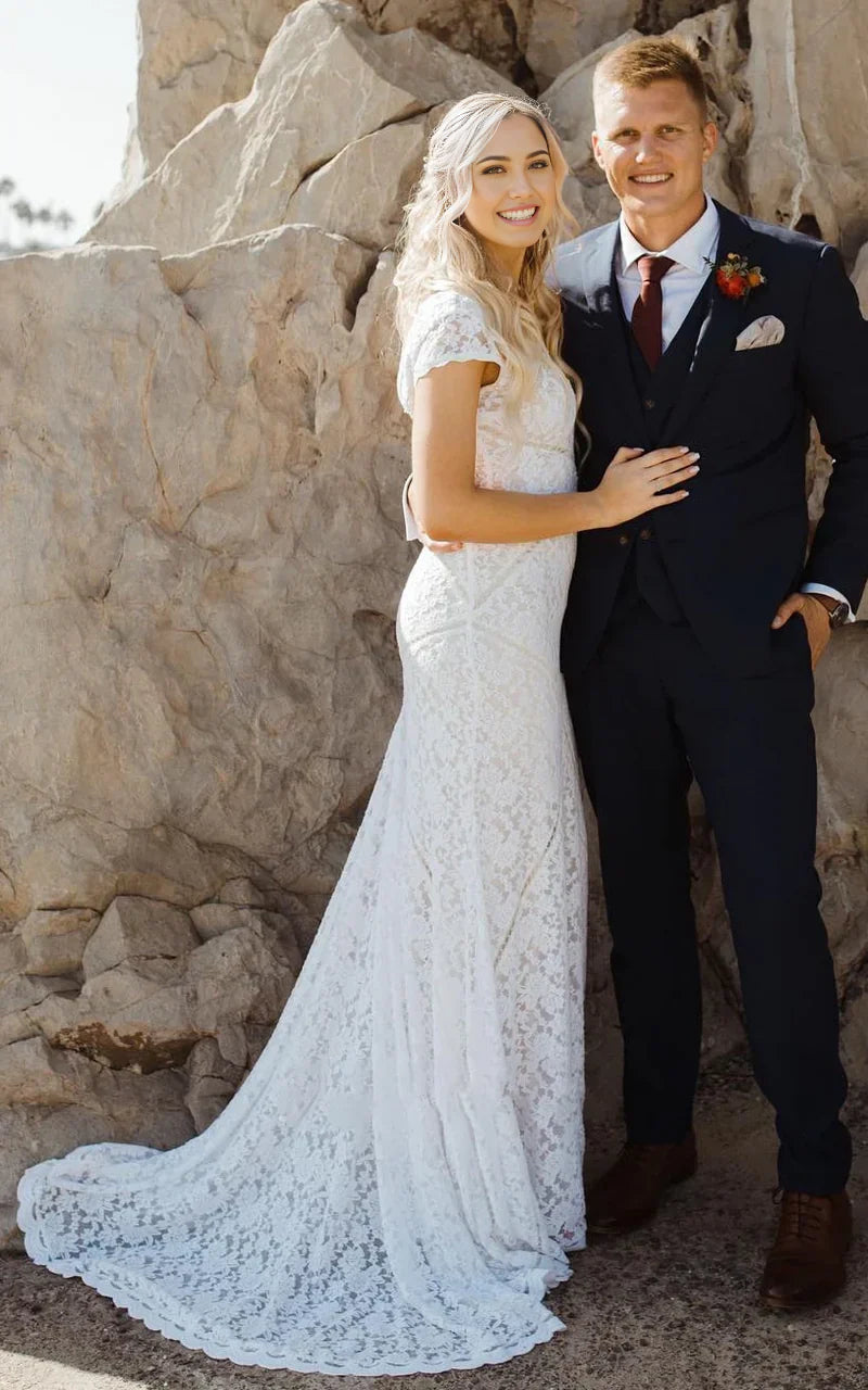 A bride wearing an elegant sheath lace wedding dress with a square V-neck and short sleeves, showcasing the sweep train.