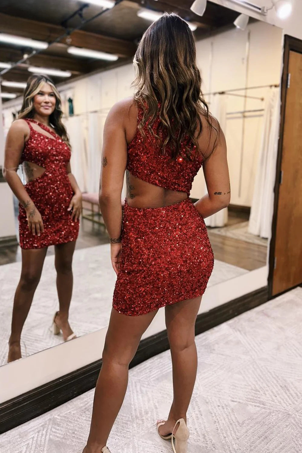 Side view of a woman wearing a red sparkly one-shoulder short prom dress.