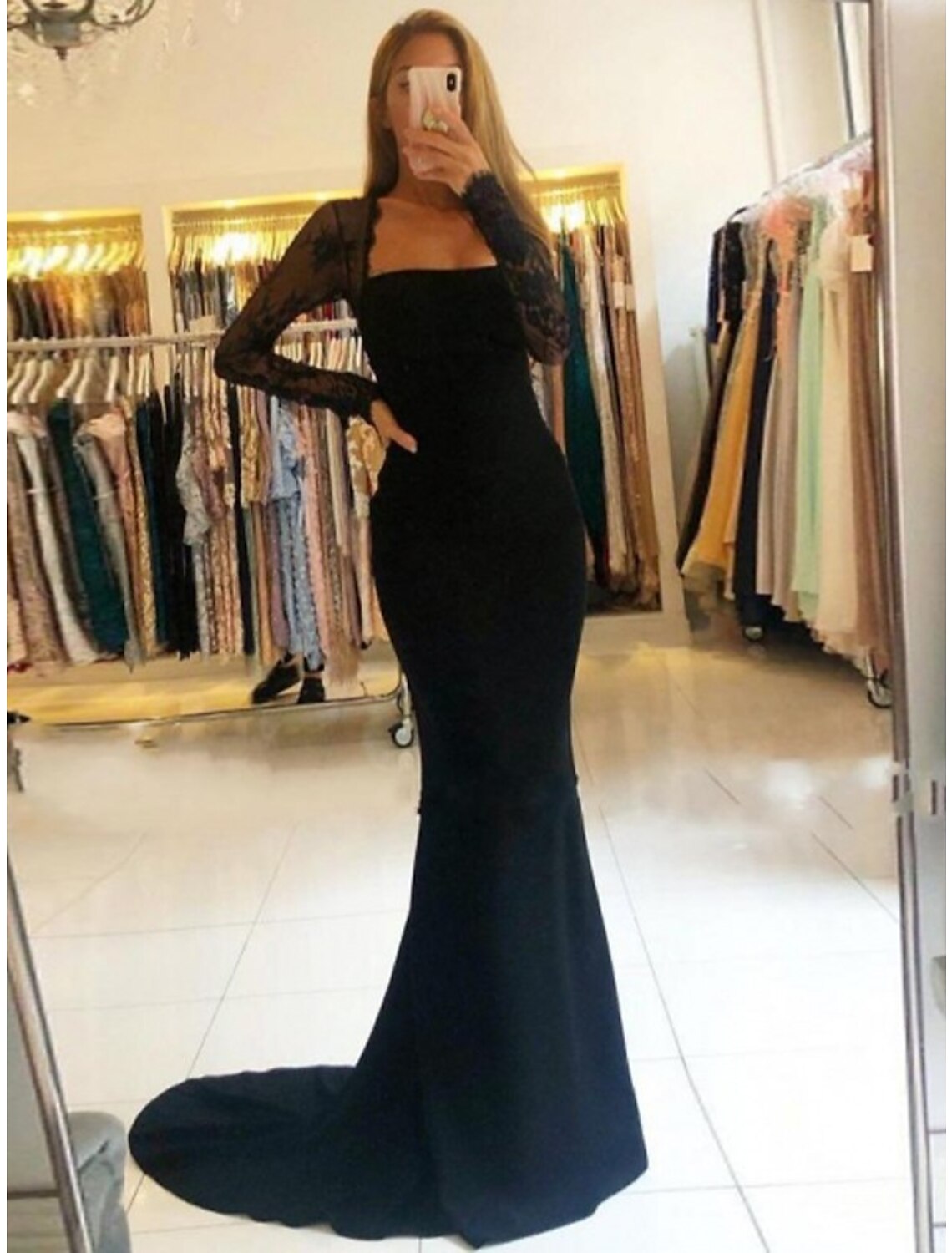 Woman modeling a strapless mermaid prom dress with beading and an open back.
