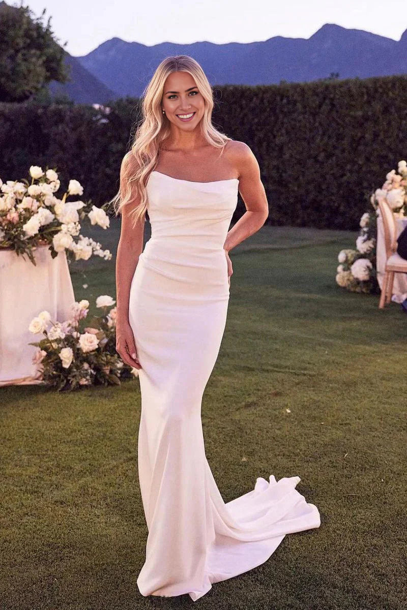 Front view of a white strapless mermaid satin wedding dress with a flowing train.